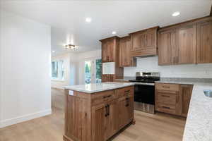 Kitchen featuring light stone counters, stainless steel electric range, a kitchen island, recessed lighting, and light wood-type flooring