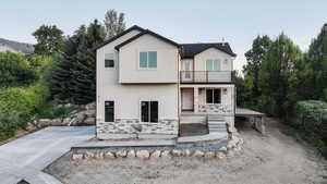 Back of house featuring stucco siding, covered porch, stone siding, and a balcony