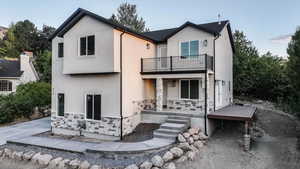 Rear view of property featuring stone siding, stucco siding, and a balcony