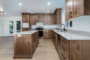 Kitchen featuring light stone counters, stainless steel appliances, a kitchen island, brown cabinetry, and recessed lighting