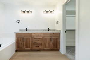 Full bathroom featuring double vanity, a garden tub, a walk in closet, and light wood-style floors