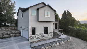 View of front of home featuring concrete driveway, an attached garage, stucco siding, a balcony, and stone siding