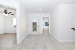 Foyer entrance with light colored carpet and a ceiling fan