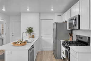 Kitchen featuring a peninsula, appliances with stainless steel finishes, light wood-style flooring, white cabinetry, and recessed lighting