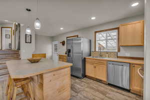 Kitchen featuring light countertops, appliances with stainless steel finishes, pendant lighting, a breakfast bar area, and a kitchen island