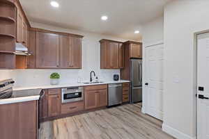 Kitchen featuring appliances with stainless steel finishes, under cabinet range hood, backsplash, light wood finished floors, and recessed lighting