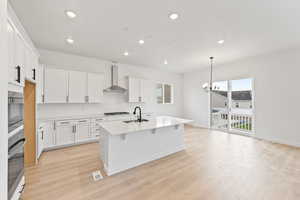 Kitchen with backsplash, white cabinetry, a kitchen island with sink, decorative light fixtures, and a chandelier