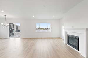 Unfurnished living room featuring light wood-style flooring, a brick fireplace, a chandelier, and recessed lighting