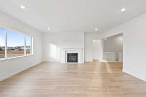 Unfurnished living room featuring recessed lighting, a glass covered fireplace, and light wood-style floors