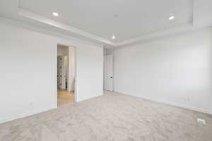 Empty room featuring a raised ceiling, light carpet, and recessed lighting