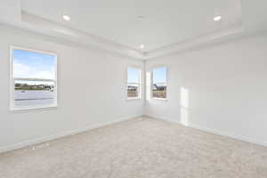 Carpeted spare room featuring a tray ceiling and recessed lighting