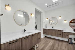 Bathroom featuring two vanities, light wood finished floors, a skylight, and recessed lighting