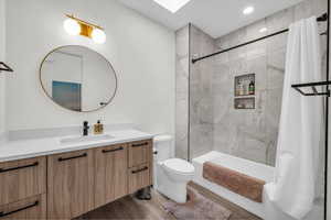 Bathroom with vanity, shower / bath combo with shower curtain, wood finished floors, and a skylight