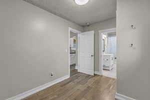 Unfurnished bedroom featuring a textured ceiling, wood finished floors, and ensuite bath