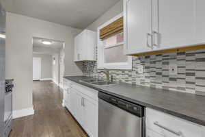 Kitchen with decorative backsplash, stainless steel appliances, dark countertops, dark wood-style flooring, and white cabinets