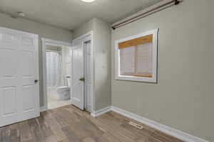 Unfurnished bedroom featuring a textured ceiling, light wood-style floors, and ensuite bathroom