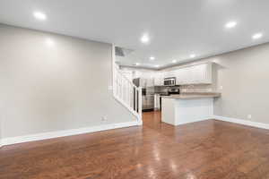 Kitchen featuring white cabinetry, open floor plan, stainless steel appliances, a peninsula, and dark wood-style flooring