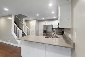 Kitchen featuring white cabinetry, a peninsula, stainless steel refrigerator with ice dispenser, dark wood-style flooring, and recessed lighting