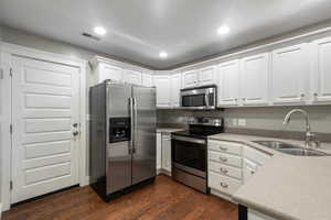 Kitchen with stainless steel appliances, white cabinets, dark wood-type flooring, recessed lighting, and light stone countertops