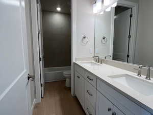 Bathroom with dark wood-type flooring, double vanity, and shower / tub combination