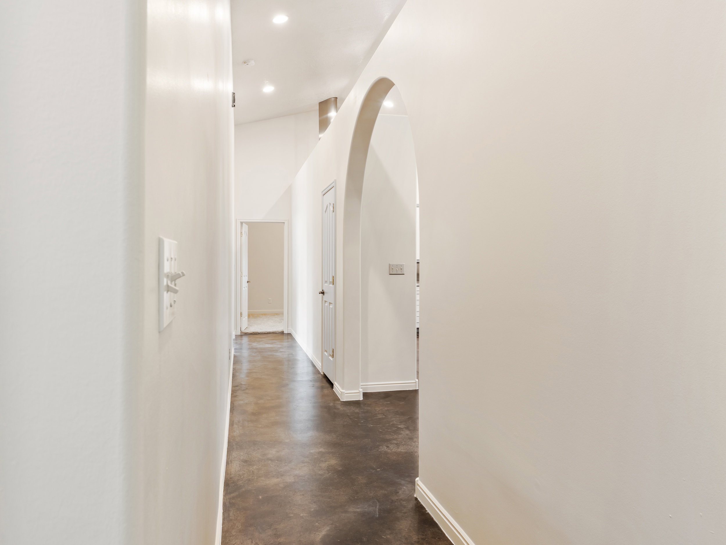 Hallway with finished concrete flooring, arched walkways, and recessed lighting
