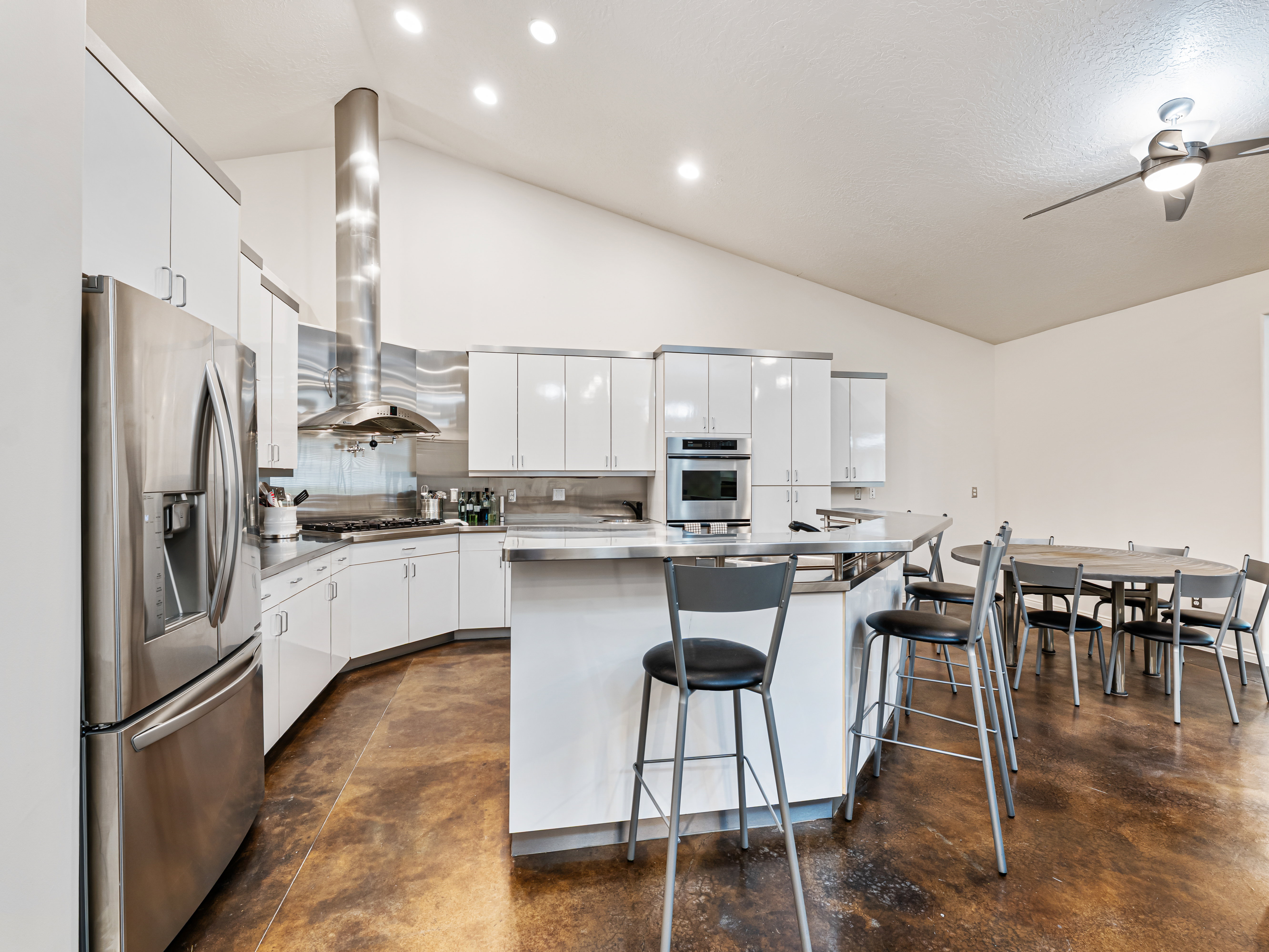 True Chef's Kitchen featuring white cabinetry, appliances with stainless steel finishes, a breakfast bar area, a ceiling fan, and a center island