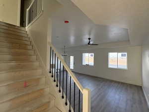 Staircase with wood finished floors, a textured ceiling, a chandelier, and ceiling fan
