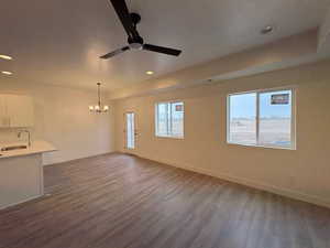 Unfurnished living room featuring suspended lighting, a ceiling fan, dark wood-type flooring, and plenty of natural light