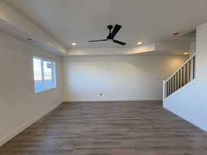 Empty room featuring dark wood-type flooring, ceiling fan, stairs, a raised ceiling, and recessed lighting