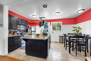 Kitchen with appliances with stainless steel finishes, a breakfast bar, dark cabinetry, and light stone countertops