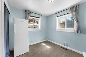 Unfurnished bedroom featuring freestanding refrigerator and carpet floors