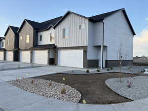 View of front of home featuring board and batten siding, a garage, driveway, and brick siding