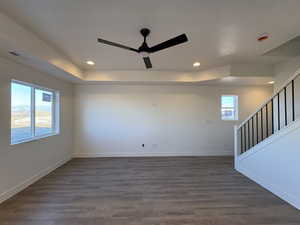 Spare room featuring dark wood-type flooring, ceiling fan, stairway, recessed lighting, and a raised ceiling