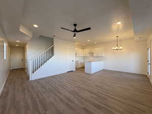 Unfurnished living room featuring recessed lighting, stairs, a chandelier, a ceiling fan, and dark wood-style flooring