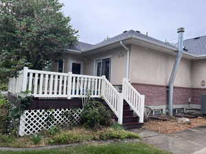 View of home's exterior with stucco siding, brick siding, a wooden deck, and a shingled roof