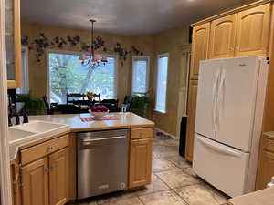 Kitchen with freestanding refrigerator, stainless steel dishwasher, hanging light fixtures, a chandelier, and light countertops