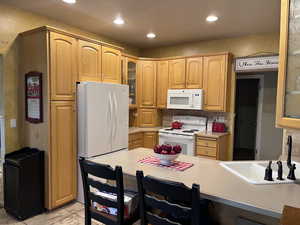 Kitchen with glass insert cabinets, white appliances, light countertops, recessed lighting, and a breakfast bar area