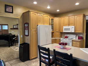 Kitchen with light countertops, white appliances, light carpet, glass insert cabinets, and recessed lighting