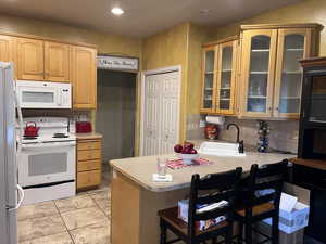 Kitchen with white appliances, light countertops, a breakfast bar, glass insert cabinets, and light tile patterned flooring