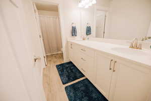 Bathroom featuring double vanity, light wood finished floors, and a shower with curtain