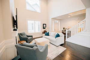 Living area featuring a towering ceiling, dark wood finished floors, a decorative wall, a wainscoted wall, and stairs