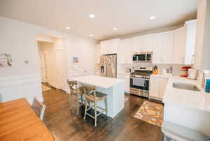 Kitchen featuring appliances with stainless steel finishes, a center island, dark wood-style flooring, a kitchen breakfast bar, and white cabinets