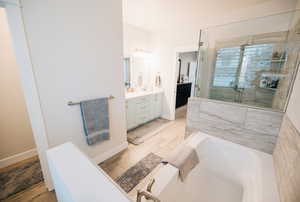 Full bath with double vanity, a bath, a shower stall, and light wood-style floors