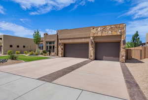 Pueblo-style home with stone siding, driveway, stucco siding, an attached garage, and a gate