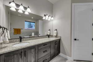 Full bath with double vanity, light marble finish floors, and a soaking tub