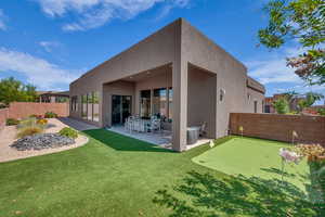 Back of house with a patio area, stucco siding, an area to practice putting, and a fenced backyard