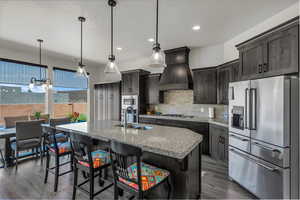 Kitchen with stainless steel appliances, hanging light fixtures, a kitchen breakfast bar, dark wood-style flooring, and tasteful backsplash