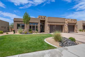 Pueblo-style house featuring stone siding, driveway, a front lawn, an attached garage, and stucco siding