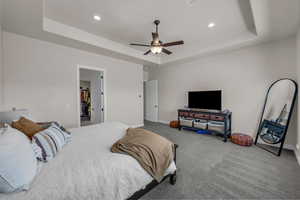 Carpeted bedroom featuring a tray ceiling, ceiling fan, recessed lighting, and a spacious closet