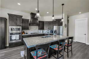 Kitchen featuring decorative backsplash, appliances with stainless steel finishes, light stone counters, a breakfast bar area, and custom exhaust hood